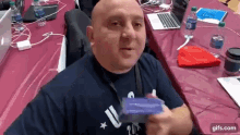 a bald man in a blue shirt is sitting at a table with bottles of water .