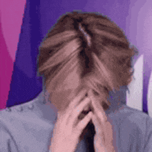 a person is covering their face with their hands in front of a purple and pink background .