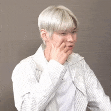 a man with white hair and a striped shirt is covering his mouth with his hand