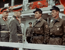 a group of men in military uniforms are standing in front of a white railing