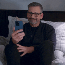 a man is sitting on a bed looking at his phone with netflix written on the bottom