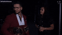 a man in a red suit is holding a wrestling belt and talking to a woman