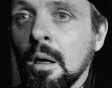 a man with a beard and a hat is making a surprised face in a black and white photo .