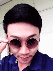a man wearing round sunglasses has a blue shirt on