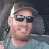 a man wearing sunglasses and a hat is sitting in a car and smiling .
