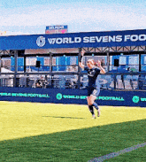 a soccer player is running on a field in front of a building that says world sevens foo