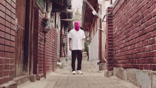 a man wearing a pink mask walks down a narrow alleyway