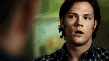 a man in a plaid shirt is making a funny face while talking to another man .
