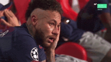 a man with a beard is sitting in a stadium with his hand to his face .