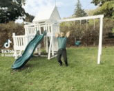 a man is standing in front of a slide and swing set with tiktok written on the bottom right