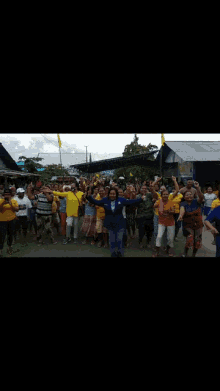 a large group of people are standing in front of a building holding their hands up in the air .