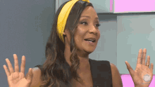 a woman wearing a yellow headband and a black top is making a gesture with her hands