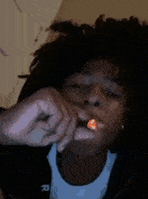a young man with dreadlocks is smoking a cigarette while wearing a black jacket with the letter r on it