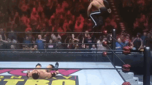 a wrestler is jumping over another wrestler in a ring with a crowd watching