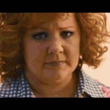 a close up of a woman 's face with red curly hair and a blue shirt .