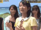 a group of young women are standing on a beach and one of them is wearing a yellow shirt
