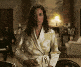 a woman in a robe stands in a room with a man sitting in the background