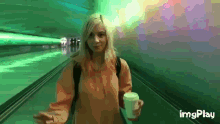 a woman is holding a cup of coffee while walking down a hallway ..