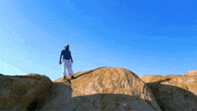 a man in a blue shirt and white pants stands on top of a rocky hill