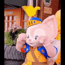 a stuffed animal wearing a crown and a blue jacket is standing in front of a brick building .