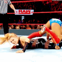 a woman is laying on the ground in a wrestling ring with a referee .