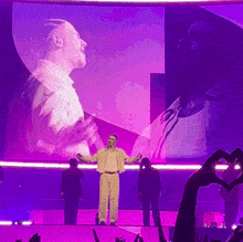a man stands on a stage with his arms outstretched in front of a large purple screen