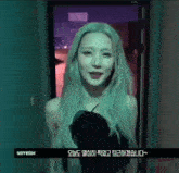 a woman with long blonde hair is standing in front of a door with foreign writing on it .