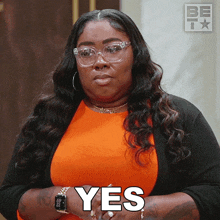a woman wearing glasses and an orange shirt says " yes "