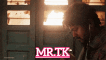 a man wearing ear buds is looking at his phone and the words mr.tk are on the screen