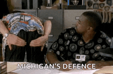 a man sitting at a desk with the words michigan 's defence written on the screen behind him