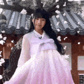 a woman in a purple dress is standing in front of a roof with flowers hanging from it