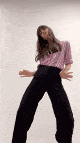 a woman in a pink and white striped shirt and black pants is dancing .