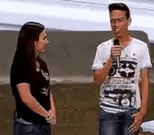 a man is speaking into a microphone while a woman looks on .