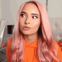 a woman with pink hair is wearing an orange sweatshirt and making a funny face .