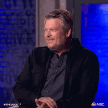 a man in a black jacket is smiling in front of a nbc screen