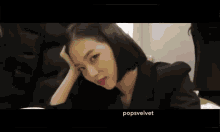 a woman in a black suit is sitting at a table with the name popsvelvet written on the bottom