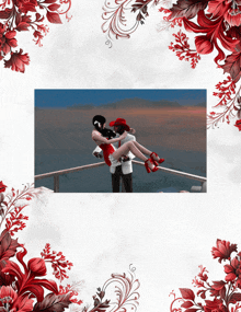 a picture of a man holding a woman in his arms with red flowers around them