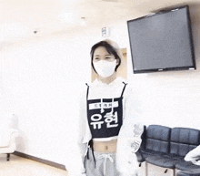 a woman wearing a mask and a crop top is standing in front of a television in a room .