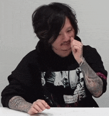 a man with a tattoo on his arm is wearing a black hoodie with a picture of a man on it