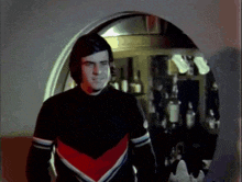 a man in a black and red sweater is standing in front of bottles