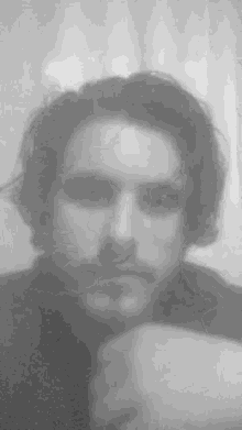 a man with long hair and a beard is taking a selfie in a black and white photo .
