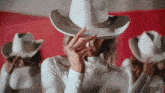 a woman wearing a white cowboy hat covering her face with her hands