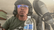 a man wearing headphones and glasses holds a bottle of water in front of a microphone