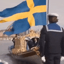 a man in a sailor uniform stands in front of a boat with a swedish flag