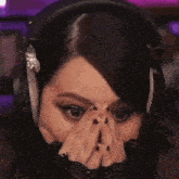 a woman wearing headphones is covering her face with her hands while playing a video game .