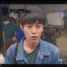 a young man wearing a denim jacket and a hat is standing in front of a camera .