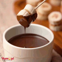 a banana is dipped into a bowl of chocolate with the words yum up below it