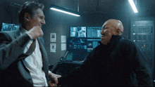 two men are standing in front of monitors and one has a poster on the wall that says wanted