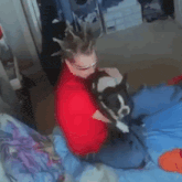 a man in a red shirt is holding a small dog