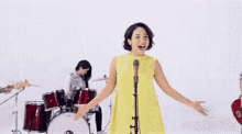 a woman in a yellow dress is singing into a microphone with a band behind her